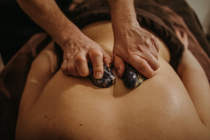 masażystka masuje plecy kobiety gorącymi kamieniami