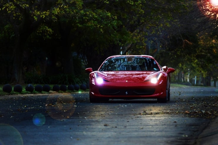 Sportowe Ferrari z włączonymi światłami, na tle natury