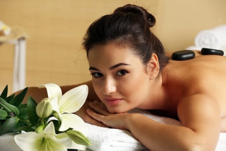 uśmiechnięta i zrelaksowana młoda kobieta na masażu kamieniami w spa
